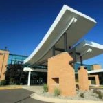 Modern building entrance with large curved white canopies supported by brick columns against a clear blue sky and glass façade behind.
